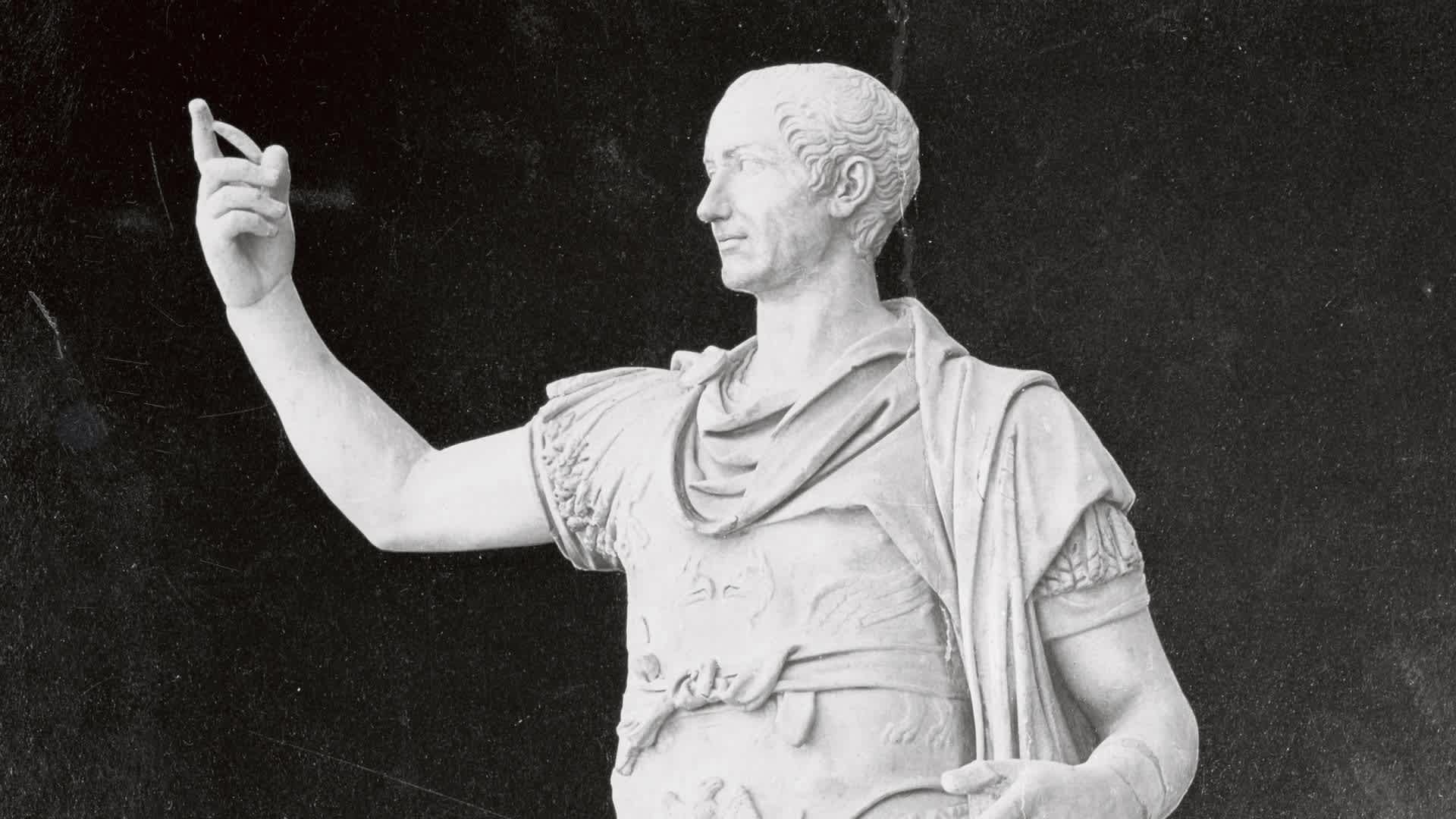 White marble statue of Roman general Julius Caesar with his right arm raised and index finger pointing upward