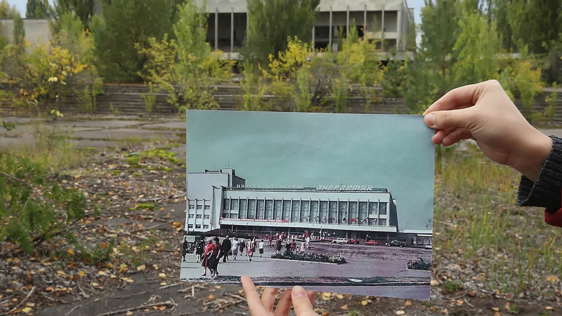 A person holds up a photo showing the city of Prypiat's main square and the 'Energetik' cultural center before the 1986 Chernobyl nuclear disaster, against the same site, now abandoned and overgrown with trees, 2015. (Credit: Sean Gallup/Getty Images)