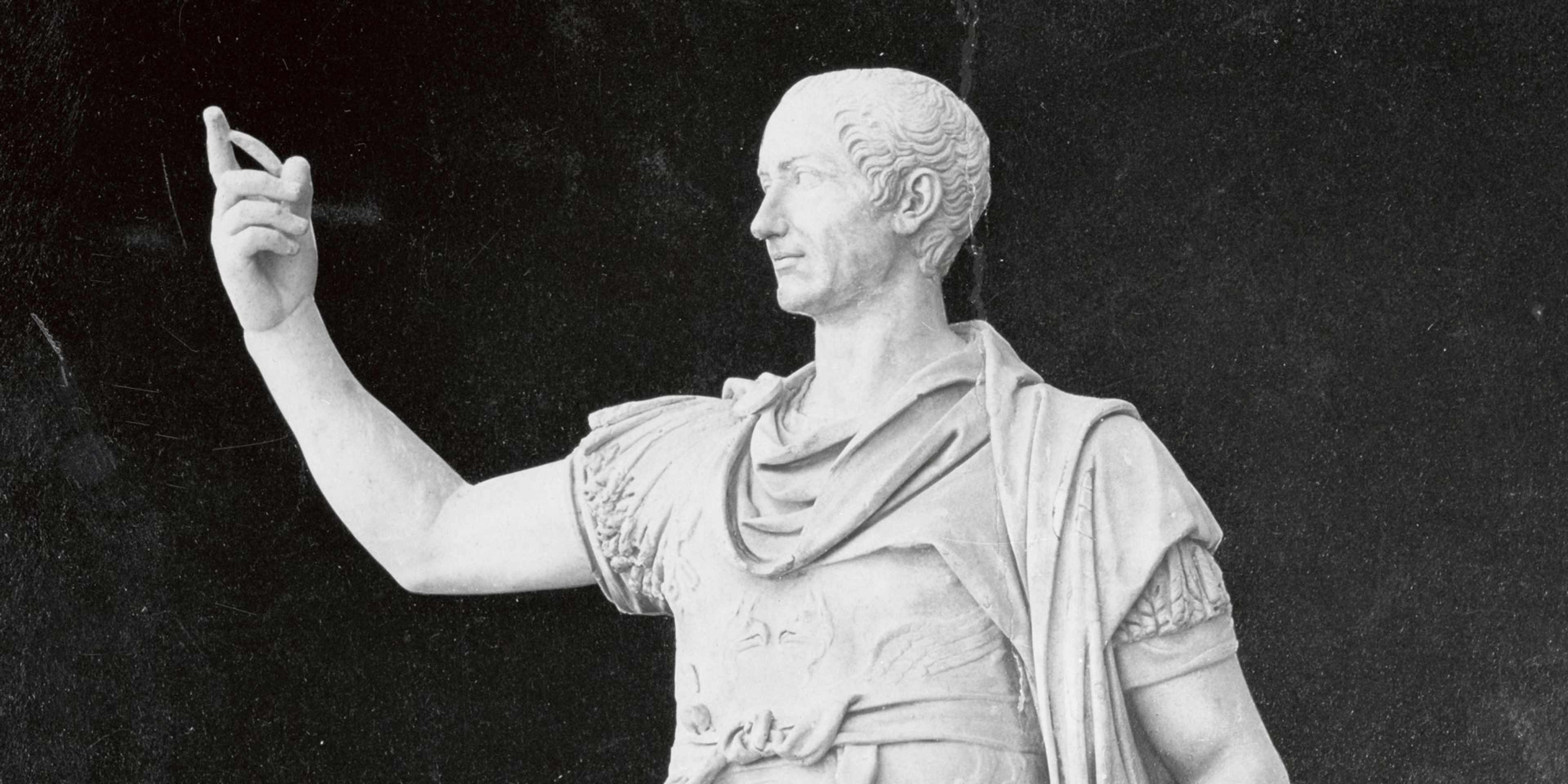 White marble statue of Roman general Julius Caesar with his right arm raised and index finger pointing upward