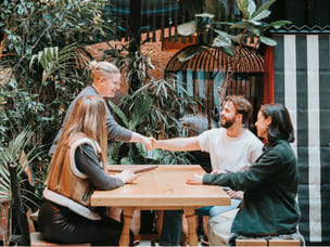 Four colleagues sitting at a table, with two of them shaking hands.  