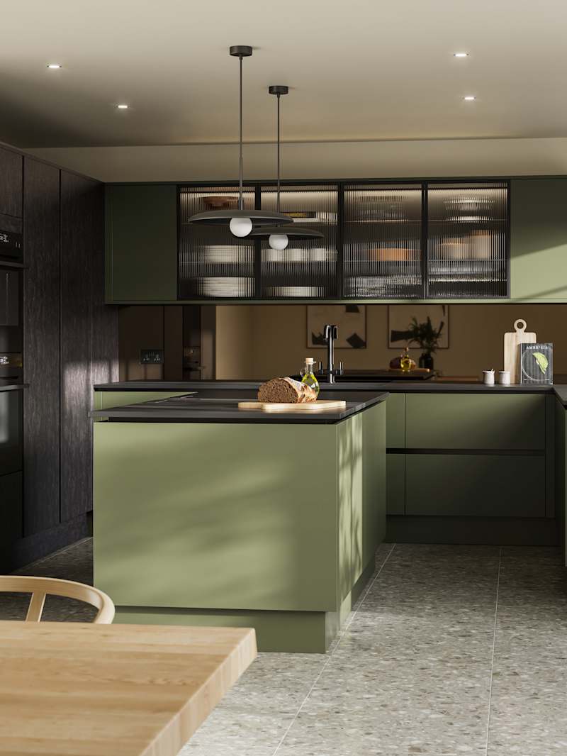 Integra Soho Tailored Green kitchen and kitchen island with contrasting dark wood Portobello Etna, black accessories, integrated ovens in tall cabinets, Dekton worktop and fluted glass vitrin wall cabinets with wood dining room table in foreground.