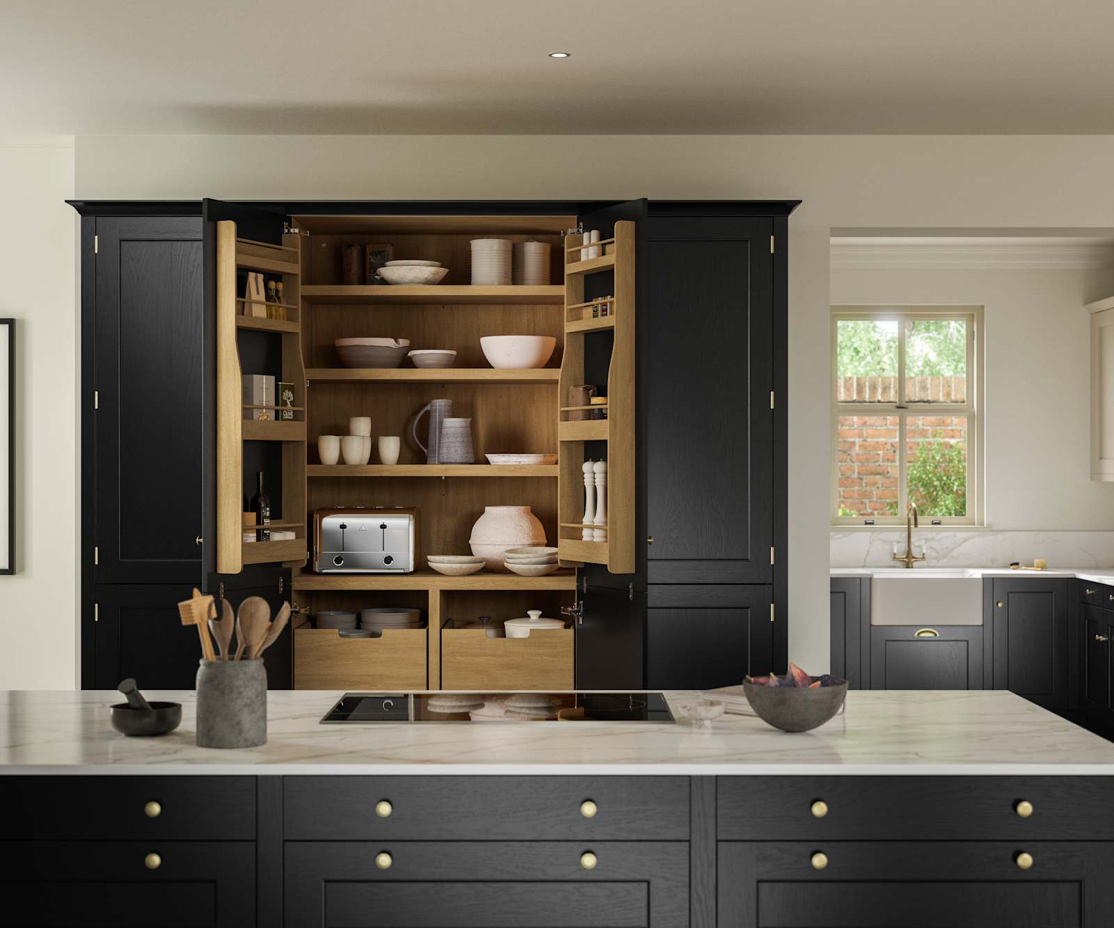 View over kitchen island in Traditional Shaker-style tactile woodgrain Ludlow Sumi Black kitchen, opened tall oak larder cabinets, brass accessories, marbled white and grey worktop, white ceramic sink and brass tap.