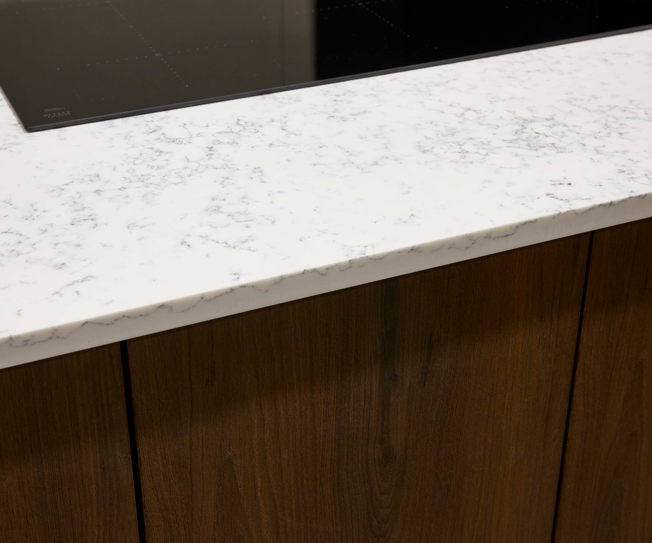 Wooden kitchen cabinets paired with white marble-effect worktop and modern glass hob.