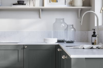 Ludlow, a traditional Shaker-style premium feel kitchen range with a visible woodgrain on its panelled doors here shown in the green shade Arboretum styled with steel knobs, steel tap, a white marbled worktop with matching splashback.