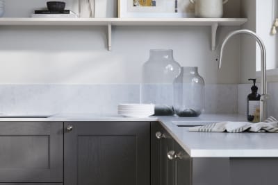 Ludlow, a traditional Shaker-style premium feel kitchen range with a visible woodgrain on its panelled doors here shown in the dark grey shade Charcoals styled with steel knobs, steel tap, a white marbled worktop with matching splashback.