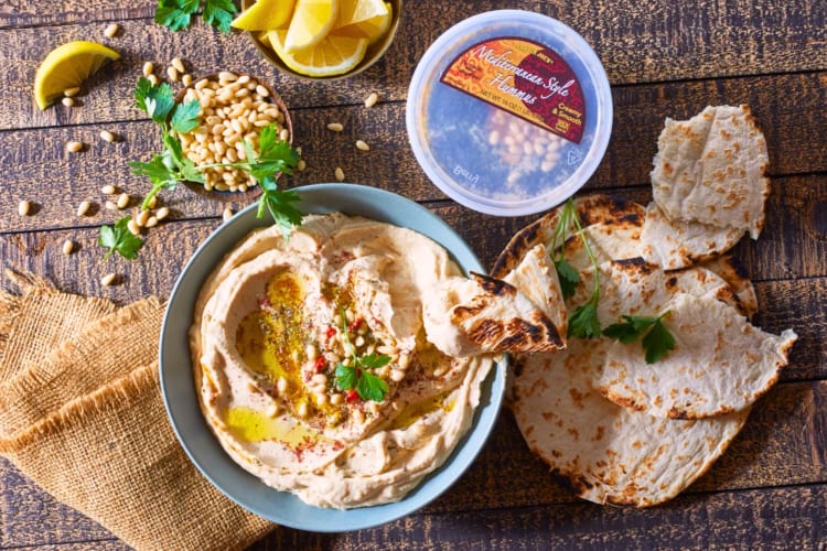 A tub and bowl of hummus next to pita and lemon slices