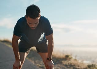 An athlete with his head down, resting his hands on his knees. He is experiencing signs of overtraining like fatigue.