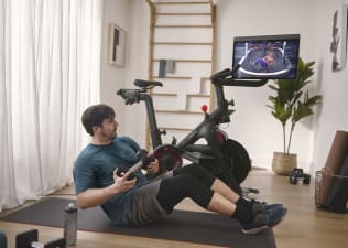 Man does a core exercise on the mat next to Peloton Bike.